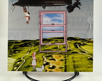 Op de afbeelding: Een collagekunstwerk met een roze raamkozijn waar een blauwe lucht met wolken doorheen zichtbaar is. Het raamkozijn is geplaatst boven een groen graslandschap met een klein figuurtje van een persoon die een kinderwagen duwt. Een boot hangt ondersteboven in de lucht boven het raamkozijn.