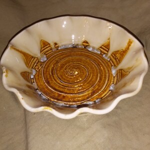 May include: A white ceramic bowl with a scalloped edge and a brown glazed interior. The interior has a spiral design.