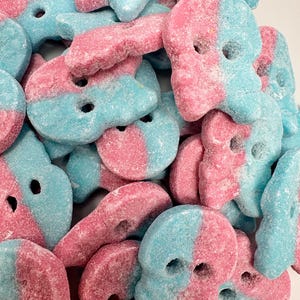 May include: A close-up of a pile of pink and blue candy shaped like skulls. The candy is covered in a white sugar coating.