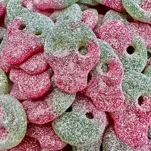 May include: A close-up of a pile of green and pink gummy candies shaped like skulls. The candies are covered in a white sugar coating.