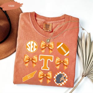 a red T-shirt with various decorative elements, including a football, a cat, and a ribbon bow, all of which are orange in color.