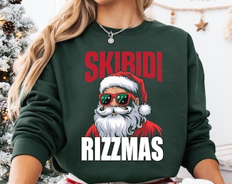May include: A forest green long-sleeve sweatshirt featuring a graphic of Santa Claus wearing red-rimmed sunglasses. The text SKIBIDI is printed in red above the graphic, and the text RIZZMAS is printed in white below the graphic.