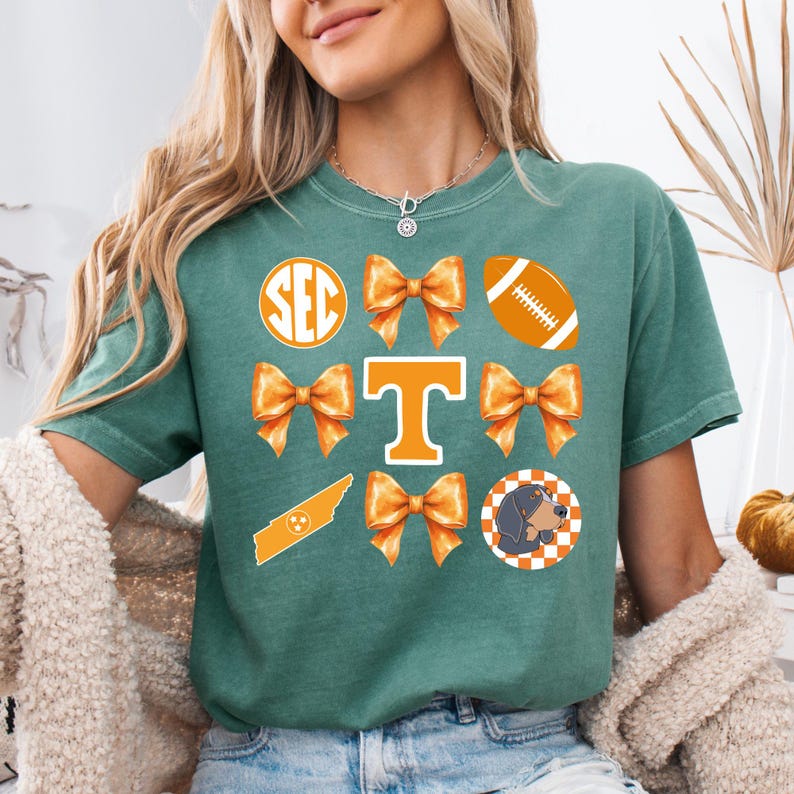 A woman wearing a green t-shirt with various orange and white graphics and text, including a football, a Tennessee state flag, and a dog.