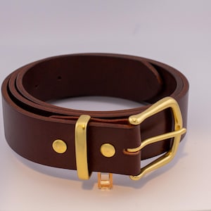 May include: A brown leather belt with a gold buckle. The belt is rolled up and the buckle is visible.