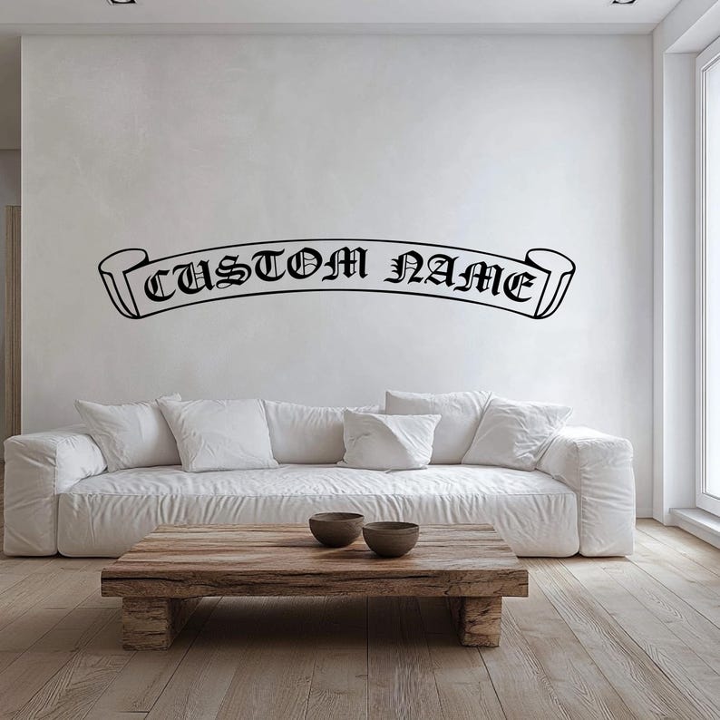 May include: A white sofa with a wooden coffee table in front of it. The wall behind the sofa has a black vinyl decal of a banner with the text "CUSTOM NAME" in a gothic font.