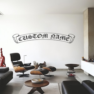 May include: Black and white wall decal with a banner design that reads "CUSTOM NAME". The decal is on a white wall in a living room setting with furniture.