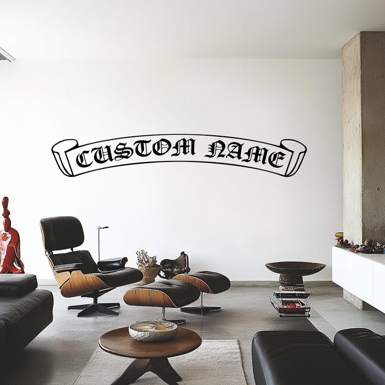 May include: Black and white wall decal with a banner design that reads "CUSTOM NAME". The decal is on a white wall in a living room setting with furniture.