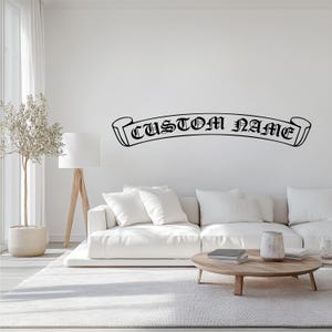 May include: A white sofa with white cushions in front of a white wall with a black vinyl decal that reads "CUSTOM NAME" in a gothic font.