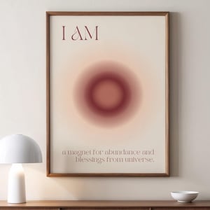 Può includere: Una stampa incorniciata con uno sfondo beige e un cerchio sfumato rosso al centro. Il testo "I AM" è in cima alla stampa. Sotto il cerchio, il testo dice "a magnet for abundance and blessings from universe."