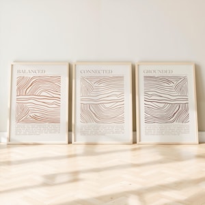 May include: Three framed art prints with beige backgrounds and brown abstract line designs. Each print has a different word at the top: "BALANCED", "CONNECTED", and "GROUNDED". Each print also has a paragraph of text below the word.