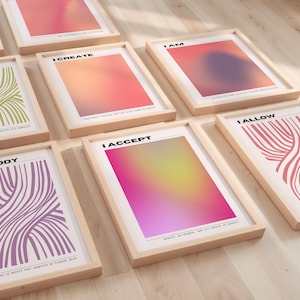 Op de afbeelding: Een verzameling ingelijste kunstafdrukken met inspirerende teksten en abstracte ontwerpen. De afdrukken tonen zinnen als "I CREATE" en "I ACCEPT" met kleurrijke gradiëntachtergronden. De frames zijn gemaakt van lichtgekleurd hout en de afdrukken worden op een houten oppervlak weergegeven.
