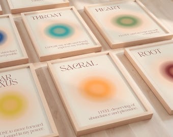 May include: A collection of framed art prints with soft, colorful aura designs. Each print features a chakra name, a corresponding affirmation, and a central, blurred color gradient. The frames are light wood, and the overall aesthetic is calming.