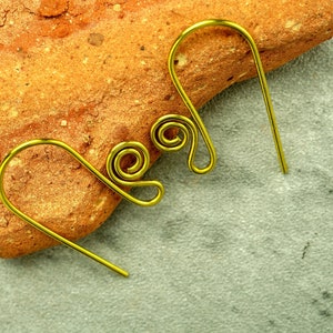 A pair of brass French hook ear wires featuring a small spiral are shown propped against a chunk of terracotta. The ear wires are compact and chunky looking. The background is a mottled grey.