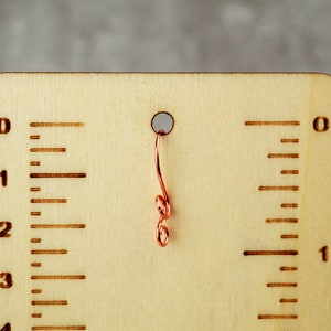 May include: A wooden measuring tool with etched markings and a copper wire accent. The tool features inch measurements, with numbers and lines indicating increments. A small hole is at the top, with a decorative copper wire hanging from it.