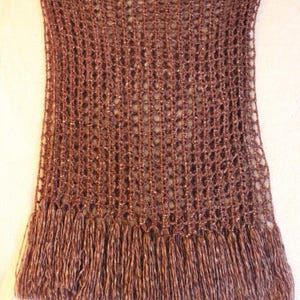 May include: A brown, open-weave crochet shawl with a fringe along the bottom edge. The shawl is rectangular and appears to be handmade. The fringe is made of the same brown yarn as the body of the shawl.