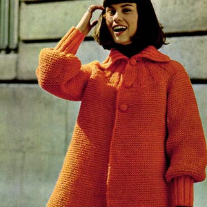 May include: An orange knit coat with a collar and button closure. The coat has long sleeves with ribbed cuffs. The person is wearing a black turtleneck and holding a black clutch. The coat is a vibrant, solid color.