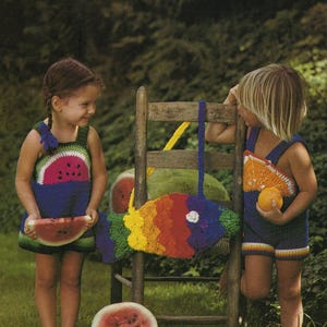 May include: Two children wearing crocheted watermelon and orange slice outfits. The child on the left is holding a slice of watermelon. The child on the right is holding an orange. A crocheted rainbow fish bag hangs on a wooden chair.