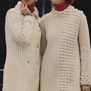 May include: Two women in cream-coloured knitted coats and hats. One coat is a long, button-down style, the other a textured, knee-length sweater dress. Both wear red polo necks. The woman on the right is wearing a red hat.