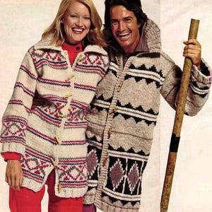 May include: Two people wearing matching cream-colored knit cardigans with geometric patterns in red, blue, and gray. The cardigans have toggle closures and are knee-length. One person is holding a wooden staff.