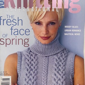 May include: Vogue Knitting International magazine cover for Spring Summer 02 featuring a person wearing a sleeveless light purple turtleneck sweater with a vertical cable knit pattern. The text reads The fresh face of spring, Moody Blues, Urban Romance, Nautical News.