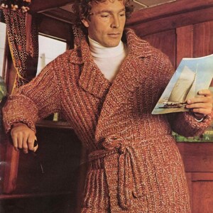 May include: A rust-colored, knitted robe with a shawl collar and a matching belt. The robe is worn over a white turtleneck. The image shows a man holding a magazine with a sailboat on the cover.