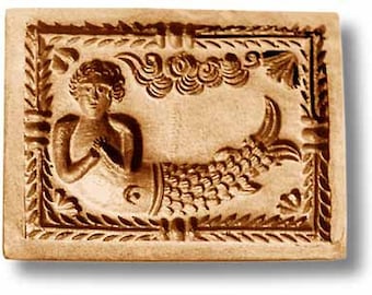 May include: A rectangular light brown wooden cookie mold featuring a carved relief of a merman with a fish tail. The figure is centered within a decorative border of leaves and scrolls, with stylized cloud patterns positioned above the figure.