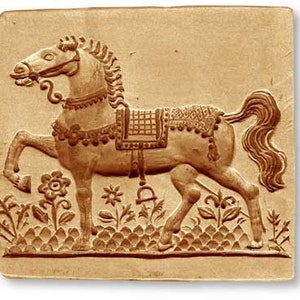 May include: A tan-colored, square relief carving of a horse in profile, adorned with decorative tack. The horse is surrounded by stylized floral and plant motifs. The carving is likely made of clay or a similar material.