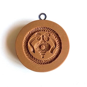 May include: A brown plastic cookie cutter shaped like a Christmas ornament with a bow. The ornament has a star in the center and a detailed design.