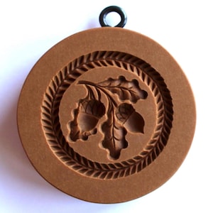 May include: Brown plastic cookie cutter with a design of three acorns on a branch with leaves. The cutter has a rope-like border around the design.