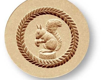 May include: A round, light brown mold with a detailed relief of a squirrel holding a nut, encircled by a laurel wreath design. The squirrel is centered within the wreath, showcasing a rustic, nature-inspired theme.