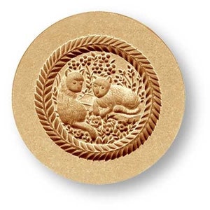 May include: A round, tan-colored wax seal stamp featuring a detailed relief of two stylized cats within a decorative border. The cats are surrounded by floral and leaf patterns, creating an ornate design.