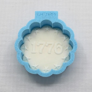 May include: A light blue scalloped cookie cutter with the text GH 7609 embossed on the top tab. The interior features a white circular insert embossed with the number 1776 surrounded by a ring of twelve small five-pointed stars.