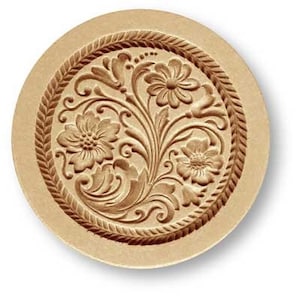 May include: A round, beige-colored cookie cutter with a raised design of a floral pattern. The design features intricate swirls and leaves, with three flowers in the center.