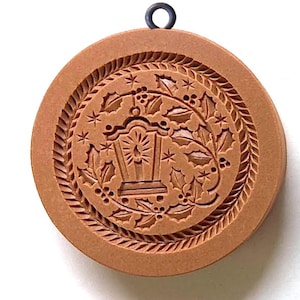 May include: A brown wooden cookie cutter with a design of a lantern and holly leaves. The cutter has a metal loop at the top for hanging.
