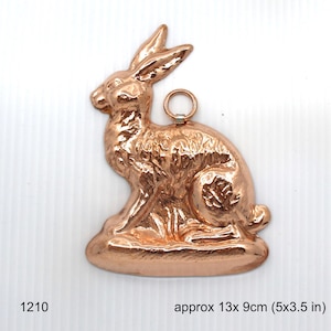 May include: A copper-colored rabbit figurine with a loop for hanging. The rabbit is sitting on a base and is approximately 13 x 9 cm (5 x 3.5 in).