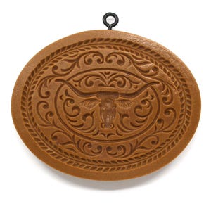 May include: Brown cookie cutter with a detailed design of a longhorn steer head with horns and a rope border.