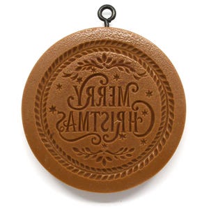 May include: A round, brown Christmas ornament with the words "MERRY CHRISTMAS" in a decorative font. The ornament has a rope-like border and a small metal loop for hanging. The design includes stars and floral accents.