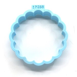 Puede incluir: Un cortador de galletas de plástico azul claro con forma de círculo y bordes festoneados. El cortador tiene el número "17288" impreso en él.