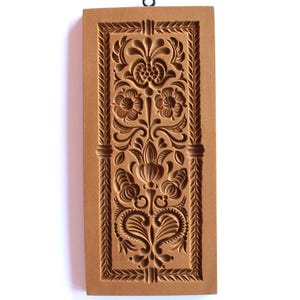 May include: A wooden cookie cutter with a floral design. The cutter is brown and has a hanging loop at the top.