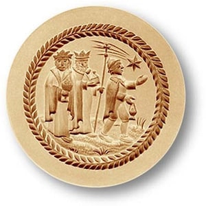 May include: A round, light brown relief carving depicting three figures in robes and crowns, with a star and a figure holding a lantern. The carving is surrounded by a detailed, brown, leafy border. The overall theme is religious.