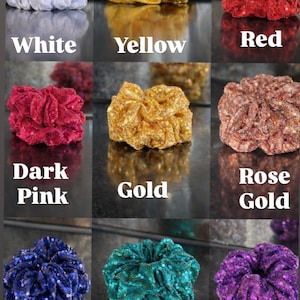 May include: Nine scrunchies in various colors, including white, yellow, red, dark pink, gold, rose gold, navy blue, green, and purple. Each scrunchie is made of a shiny, textured fabric and is displayed with its color name below.