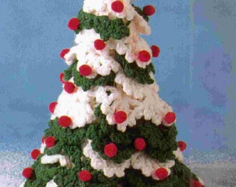 May include: A handmade crochet Christmas tree. The tree features alternating layers of white and green yarn, with red pom-poms scattered throughout. The tree is set against a light blue background, creating a festive holiday decoration.