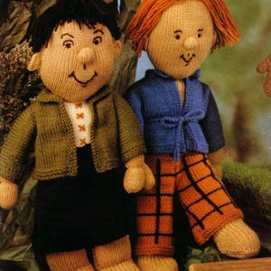 Puede incluir: Dos muñecos tejidos a mano. Uno lleva una chaqueta verde, una falda negra y una camisa blanca. El otro lleva una chaqueta azul y pantalones a cuadros naranjas. Ambos muñecos tienen piel bronceada, pelo negro y naranja y caras sonrientes.