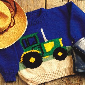May include: A blue knitted jumper with a green and yellow tractor design. The jumper has a cream-coloured bottom and a round neckline. A straw hat and a pair of blue wellington boots are also in the image.
