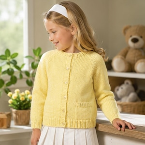 May include: A pale yellow long-sleeved knit cardigan featuring a round neckline, a vertical row of five small white buttons down the centre, and two square patch pockets on the lower front. The garment has ribbed cuffs and a ribbed hemline.