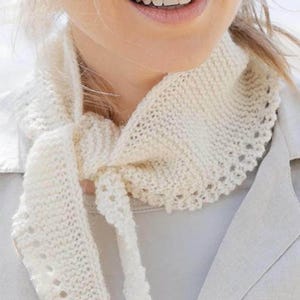 May include: Cream-colored knitted scarf with a scalloped edge and tie closure. The scarf is made of a soft, textured yarn and is worn around the neck. The design features a delicate openwork pattern along the edges, adding a touch of elegance.