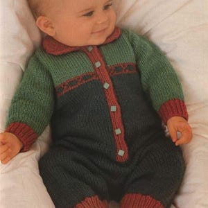 Op de afbeelding: Gebreide babyromper in groen en marineblauw, met rode accenten op de kraag, manchetten en knoopsluiting. De romper heeft een decoratief patroon over de borst en is vastgemaakt met vierkante, lichtblauwe knopen.