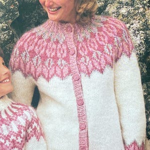 May include: A white and pink knitted cardigan with a button-up front. The cardigan features a patterned yoke and cuffs in shades of pink and white. The design includes a zig-zag pattern at the bottom and cuffs.