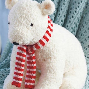 May include: A soft polar bear toy with a white, fluffy body and a red and white striped scarf. The bear has small black eyes and ears. The toy is sitting on a light blue surface.