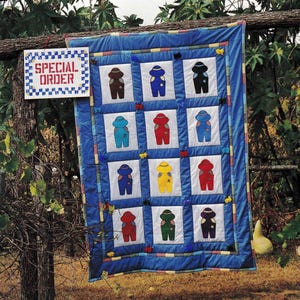 Puede incluir: Un edredón hecho a mano con un borde azul y un patrón repetido de figuras de varios colores. Cada figura lleva un sombrero y un peto. Un letrero que dice "SPECIAL ORDER" está cerca.